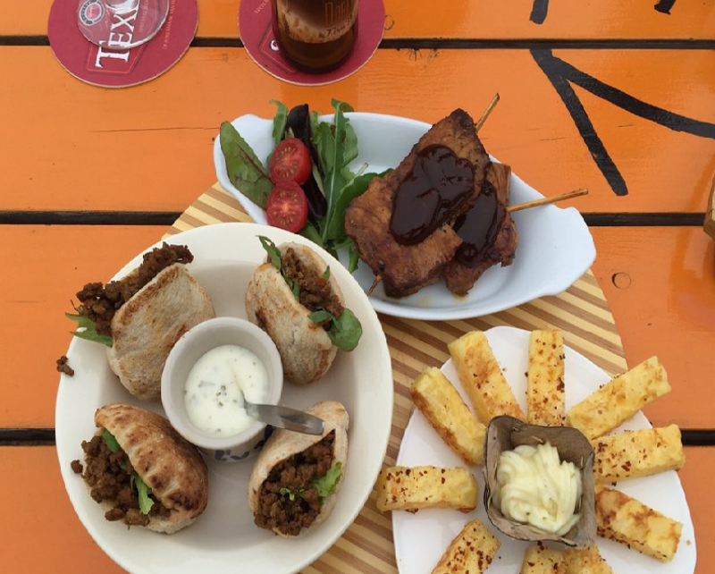 Kleine gerechtjes om te delen op de oranje picknicktafel: pita, ribbetjes en halloumifriet
