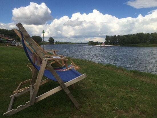 Ligstoelen in het gras aan de Maas, het veerpontje op de achtergrond