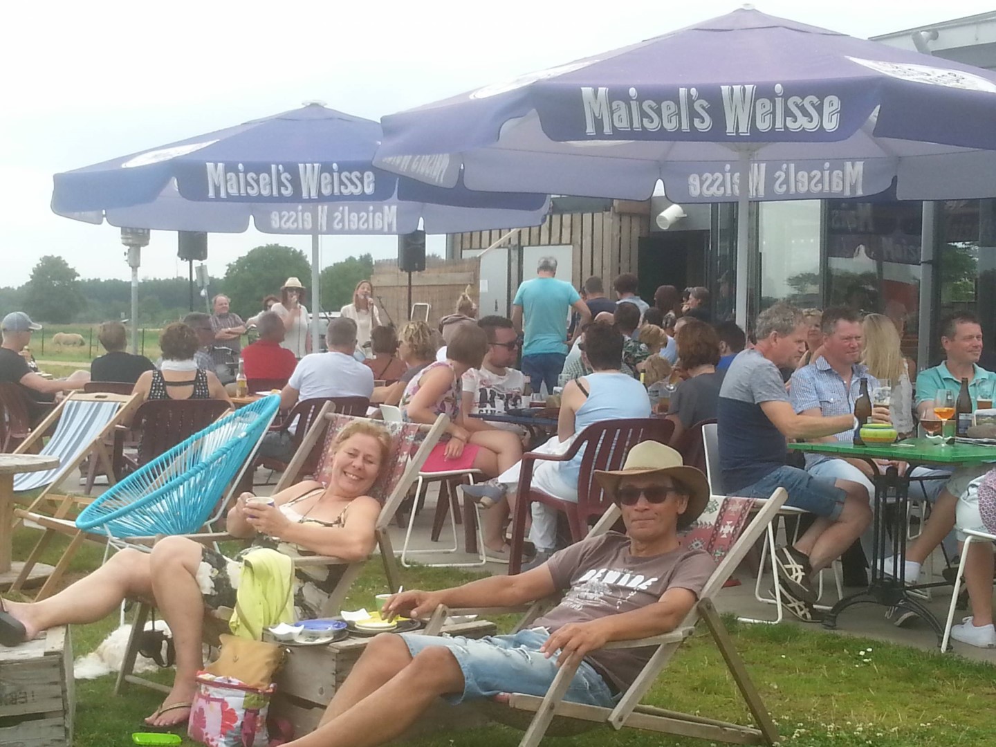 Ligstoelen in het gras bij Hoëg, parasols en livemuziek aan de Maas
